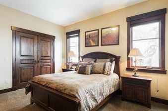A cozy bedroom at Silver Star 4202 features a large bed with a patterned comforter, dark wood furniture, and two landscape paintings above the headboard, with natural light filtering through a window.