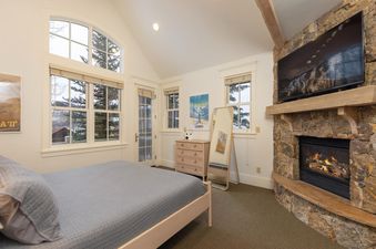 The bedroom in The Victorian features a comfortable bed, a stone fireplace, and large windows offering views of the snowy landscape.