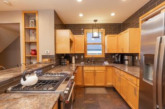 A spacious and well-lit kitchen featuring light wood cabinetry, dark tiled backsplashes, and granite countertops.