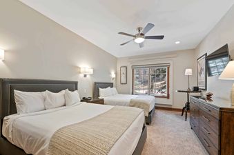 A comfortable bedroom at The Charter G1305 featuring two full beds, a ceiling fan, and a large window with an outdoor view.