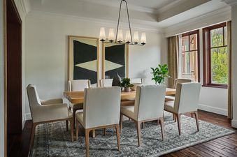 An elegant dining room in the Montage Three Bedroom Residence Resort View features a large wooden dining table surrounded by cream-colored upholstered chairs, with two large abstract paintings on the wall and a modern chandelier overhead.