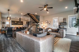 A modern open-concept living space with a kitchen, dining area, and lounge, featuring an open-riser staircase and contemporary furnishings.