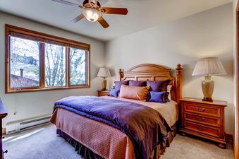 Cozy bedroom at Christie Club 316 featuring a queen bed with purple and coral bedding, wooden furniture, and a large window.