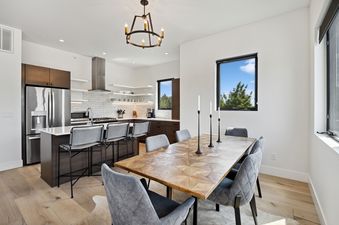 A modern open-concept kitchen and dining area with a wooden table, upholstered chairs, and sleek appliances.