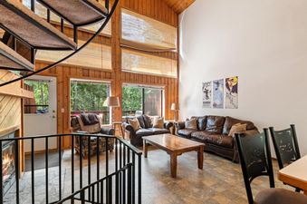 The expansive living room at Ptarmigan Hideout is designed for comfort and style, featuring vaulted wooden ceilings, large windows, and a spiral staircase.