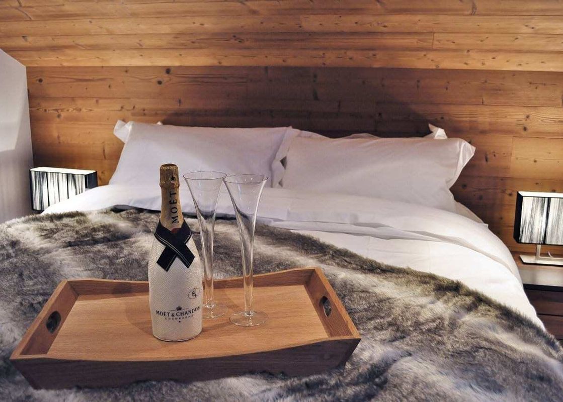 A cozy bedroom at Northern Lights 32 with a bed made with white linens and a faux fur throw, a wooden headboard, and a wooden tray with champagne and two flutes.