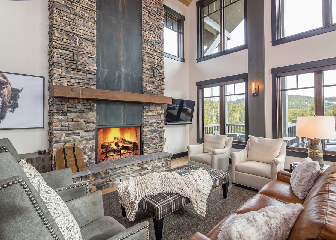 A cozy and elegant living room at 7 Lower Cascade Ridge features a stone fireplace, plush seating, and large windows with scenic outdoor views.