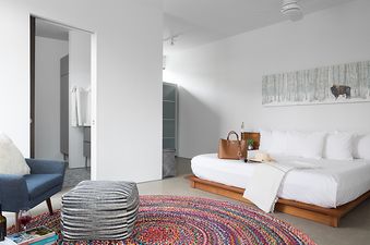 Bright master bedroom at Taminah Retreat with a platform bed, vibrant round rug, and blue armchair.