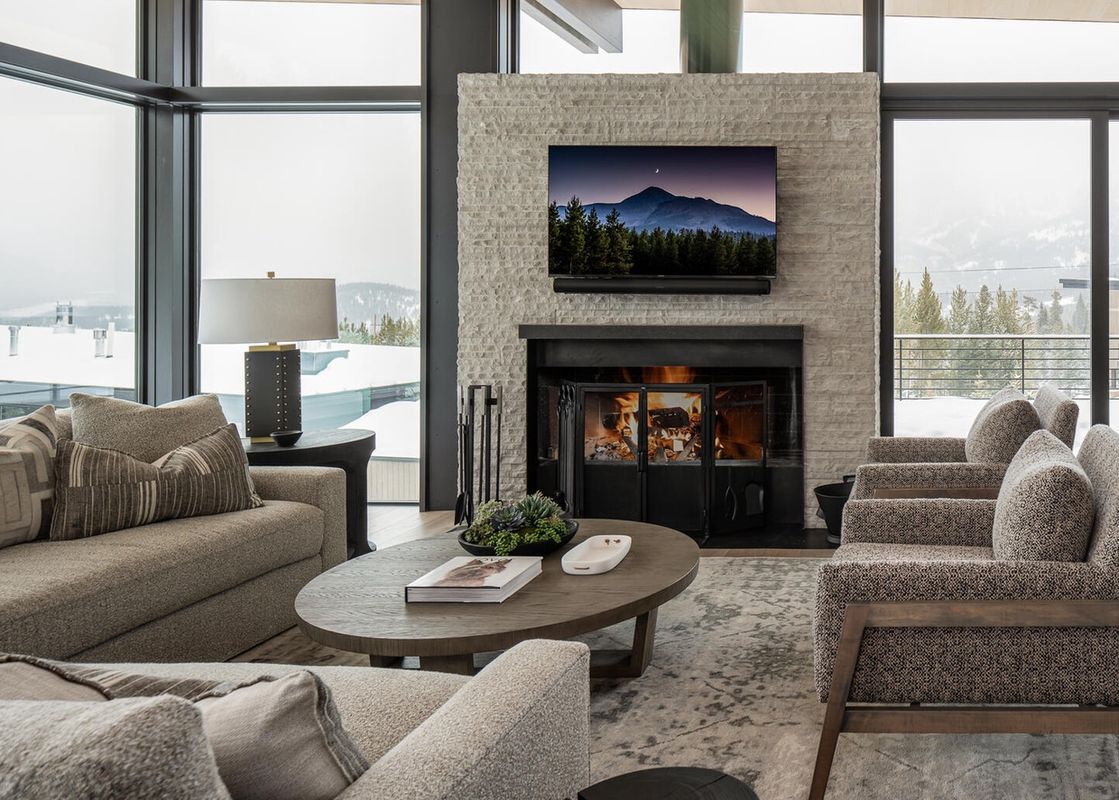 Spacious living room in Moonlight Basin 5 Thistle Way, featuring a cozy fireplace, plush furniture, and a stunning view of a snow-covered mountain landscape.