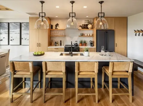 A modern kitchen and dining area in The Sylvan Lodge One Bedroom Suite, featuring a marble island, wooden cabinetry, and contemporary lighting.