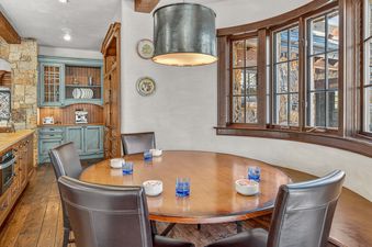A rustic yet elegant dining area in High Road features a round wooden table with leather chairs, illuminated by a hammered metal pendant light.