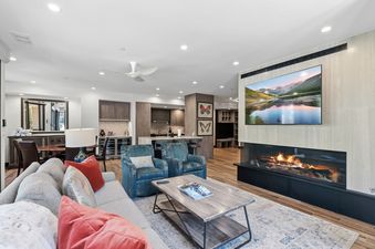 A modern, open-concept living room with a large fireplace, comfortable seating, and a view into the kitchen area.