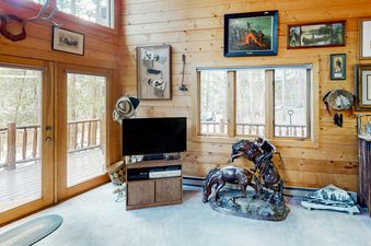 Atkins Cabin has a living area with a large television and a comfortable-looking couch and two wooden chairs.