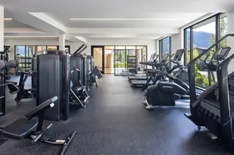 A wide view of a modern fitness center with various exercise machines, including treadmills, ellipticals, and strength equipment, all set on a black rubber floor with large windows offering mountain views.