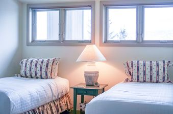 A twin bedroom at Snowridge 2 with two single beds, a bedside table, and large windows.