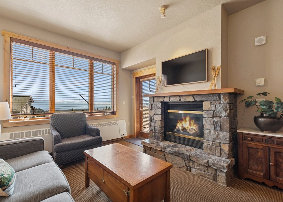 A cozy living room in Morning Eagle 207 features a stone fireplace, a flat-screen TV, comfortable seating, and a large window offering scenic mountain views.