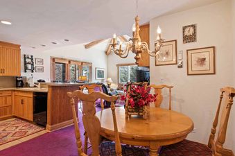 A cozy dining area at The Charter E2205 featuring a round wooden table, matching chairs, a chandelier, and an open layout connecting to the kitchen and living space with views of the outdoors.