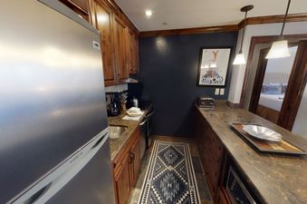 The kitchen of Manor Vail 280 is compact and features dark wooden cabinets, granite countertops, a full-size refrigerator, and a breakfast bar.