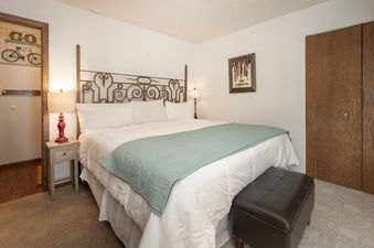 The bedroom at Silverado II Unit 334 features a king-sized bed with a wrought iron headboard and white bedding, complemented by a light teal throw.