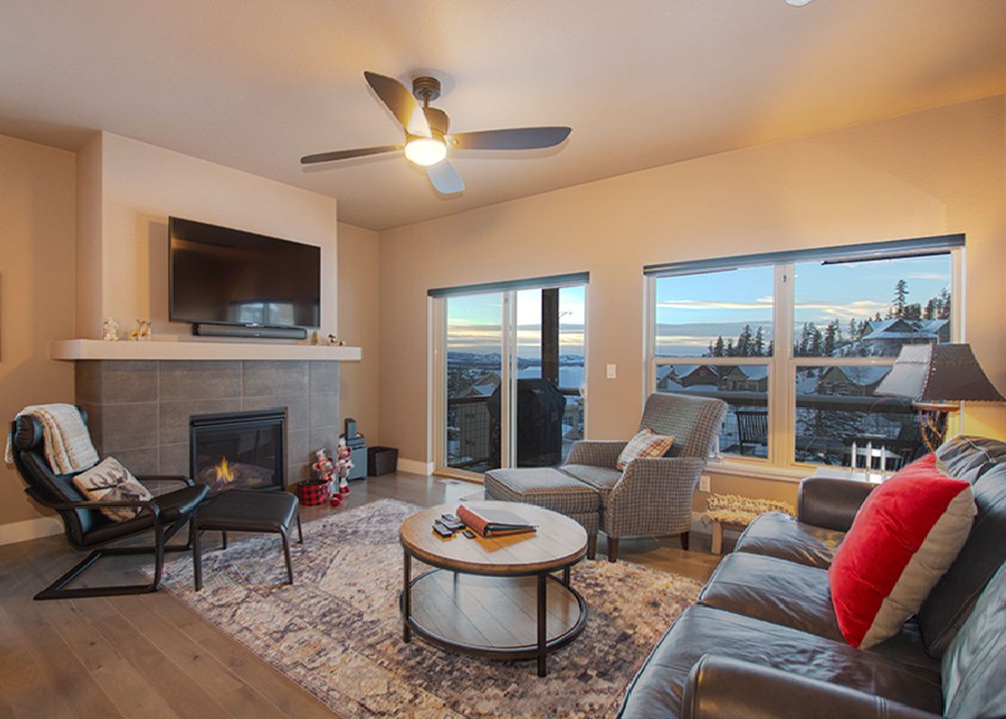 The living area of Rendezvous 47 Lookout Point boasts comfortable seating around a fireplace and a large television, with expansive windows offering views of the snowy landscape outside.