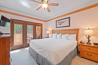 A master bedroom at The Charter D3705 featuring a king-sized bed with white linens, wooden furniture, and two glass-paned doors leading to a private balcony.