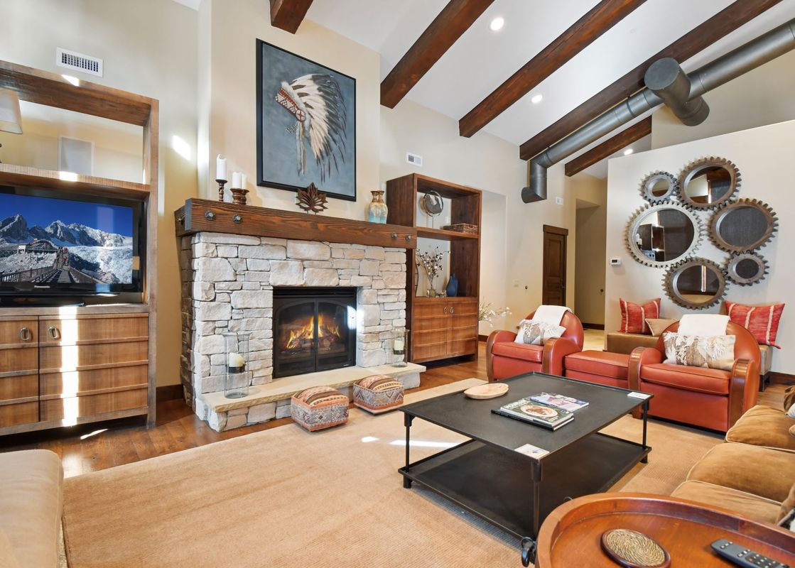 A cozy living room at Silver Star 4303 features a stone fireplace, exposed wooden beams, and comfortable seating with a large flat-screen TV.