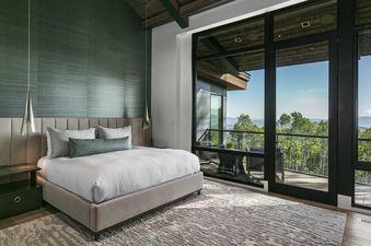 A luxurious bedroom at Moonshadow 8927, featuring a large bed with a beige upholstered headboard, white bedding, and accent pillows, positioned against a textured dark green wall.