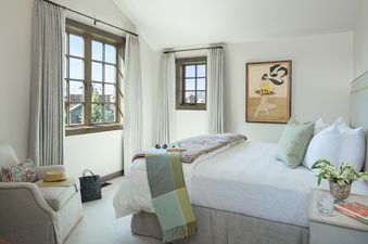 A serene bedroom at Four Pines 12, featuring a neatly made bed, a comfortable armchair, and large windows with light curtains, offering a peaceful retreat.