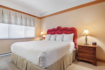 A cozy bedroom at The Charter G0505 with a king-sized bed, red tufted headboard, and wooden nightstand with a lamp.