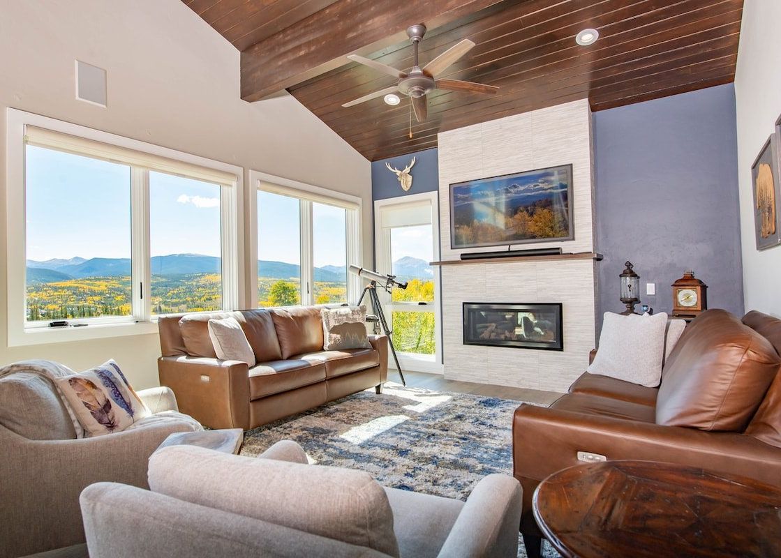 Cozy living room in Peak View Paradise featuring leather sofas, a modern fireplace, and large windows with scenic mountain views.