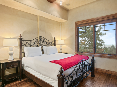 The bedroom in Grand Lodge Studio 204 features a king-size bed, a red throw blanket, and a window with a view of the mountains.