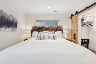 A cozy bedroom with a king-sized bed, white bedding, blue and white pillows, and winter garland decorations, featuring a barn door leading to a closet.