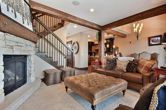 A cozy living room in Silver Star 903 with a large leather sofa and ottoman, a stone fireplace, and rustic wooden beams leading into a kitchen.