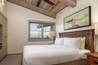 Top of the Village Slope 408's bedroom features a king bed with white linens, two lamps on nightstands, a wooden headboard, and a window with a mountain view.