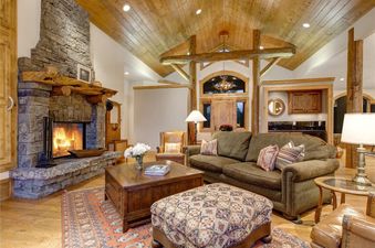 Rustic living room with a stone fireplace, wood ceiling, and green sofa at Sweetwater Jackson Hole.