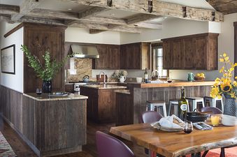 A rustic yet elegant kitchen and dining area in Four Pines 07, featuring dark wood cabinetry, granite countertops, exposed wooden beams, and a live-edge dining table.