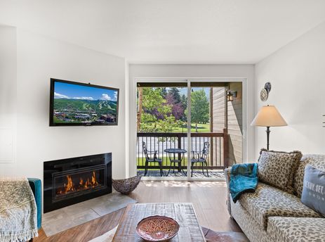 A cozy lounge area with a fireplace, television, and a leopard print sofa, leading out to a balcony with outdoor seating.