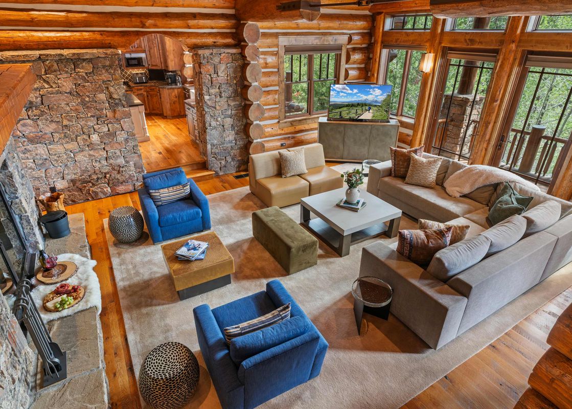 A high-angle view of the spacious, rustic living room at Timber Ridge at Jackson Hole, featuring comfortable seating and a large stone fireplace.