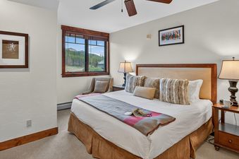 A cozy bedroom at Crystal Peak Lodge 7407 with a large bed, nightstands with lamps, a window with mountain views, and framed artwork.