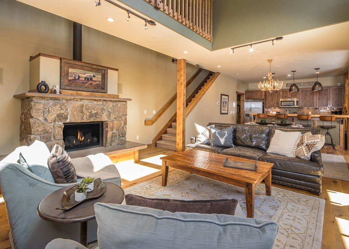 A cozy living room with a stone fireplace, leather sofa, and an open-concept kitchen with a breakfast bar.