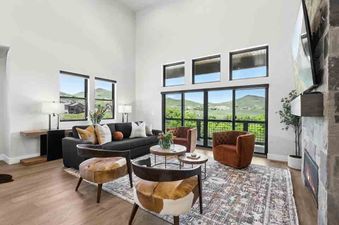 A living room with a large sectional couch, two accent chairs, and a coffee table. The room has large windows with views of a mountain range.