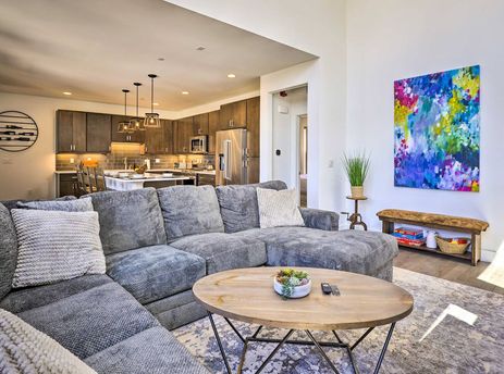 The open-concept living area and kitchen of Rendezvous Retreat, featuring a large gray sectional sofa, a wooden coffee table, and a modern kitchen with dark cabinetry and stainless steel appliances.