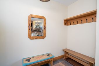 A functional and inviting entryway and mudroom with a rustic wooden mirror reflecting the kitchen, a wooden bench with duck artwork, and a wooden shelf with hooks.