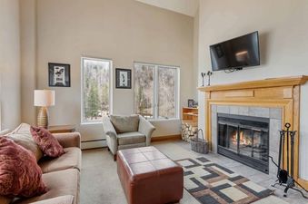 A cozy living room at The Charter L332 with a fireplace, comfortable seating, and large windows offering a view of the outdoors.