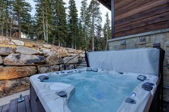 An inviting outdoor hot tub at Ruby Run with bubbling water, set on a wooden deck surrounded by a stone retaining wall and pine trees.