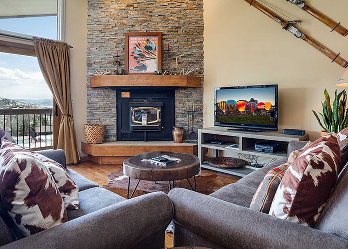 A cozy living room at the Ranch at Steamboat RA304 with a fireplace, a mounted television, and a window offering a snowy exterior view.