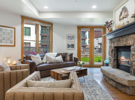 The living area at 118 Villa Montane features a plush brown leather sofa, inviting armchairs, and a stone fireplace, creating a cozy and stylish retreat.