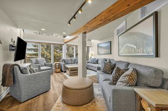 The image shows the living area at Lowell Slopeside 260, featuring a spacious layout with comfortable seating, large windows offering natural light and views of trees, and elegant decor.