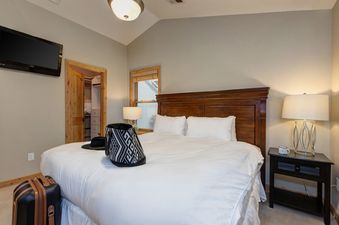 The bedroom features a king bed with soft white linens and a wooden headboard.