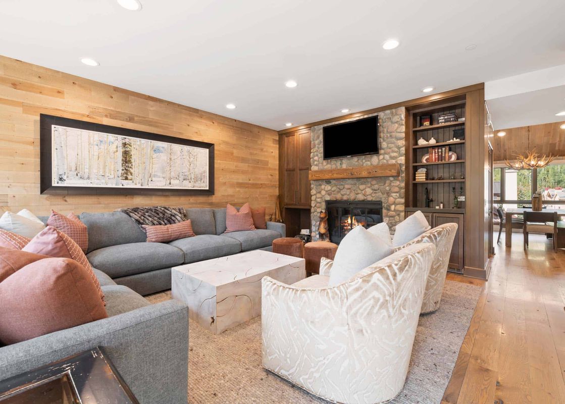 The inviting living area features a stone fireplace, a large gray sectional sofa with pink accent pillows, and light wood paneled walls.